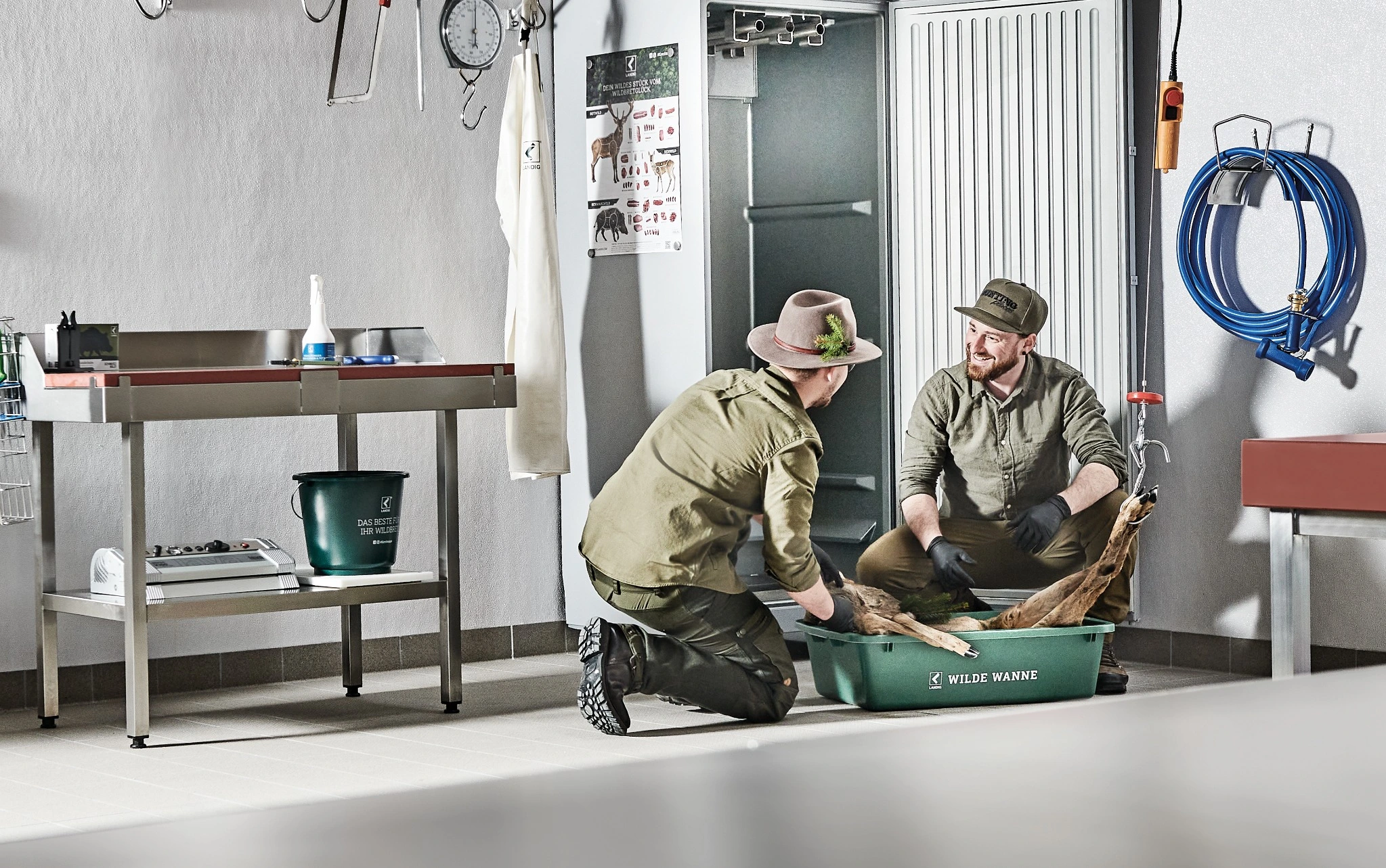 Jäger bei der hygienischen Wildverarbeitung vor einem geöffneten Wildkühlschrank im Wildraum mit Edelstahl-Arbeitsplatz und Zubehör zur Wildkühlung.